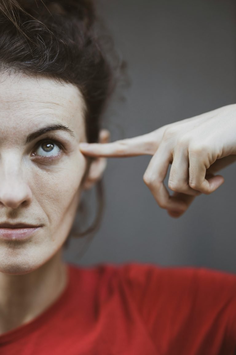 a woman in a red tshirt with her index left finger pointing to her left eye to show she's focusing