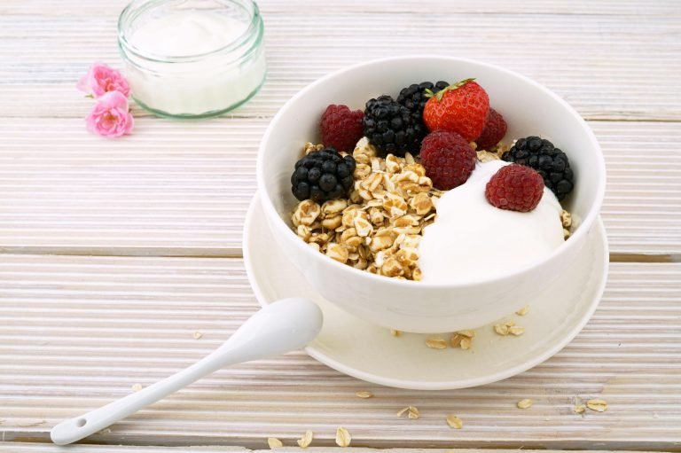 A white bowl with oats, muesli and berries, with some white yogurt on top