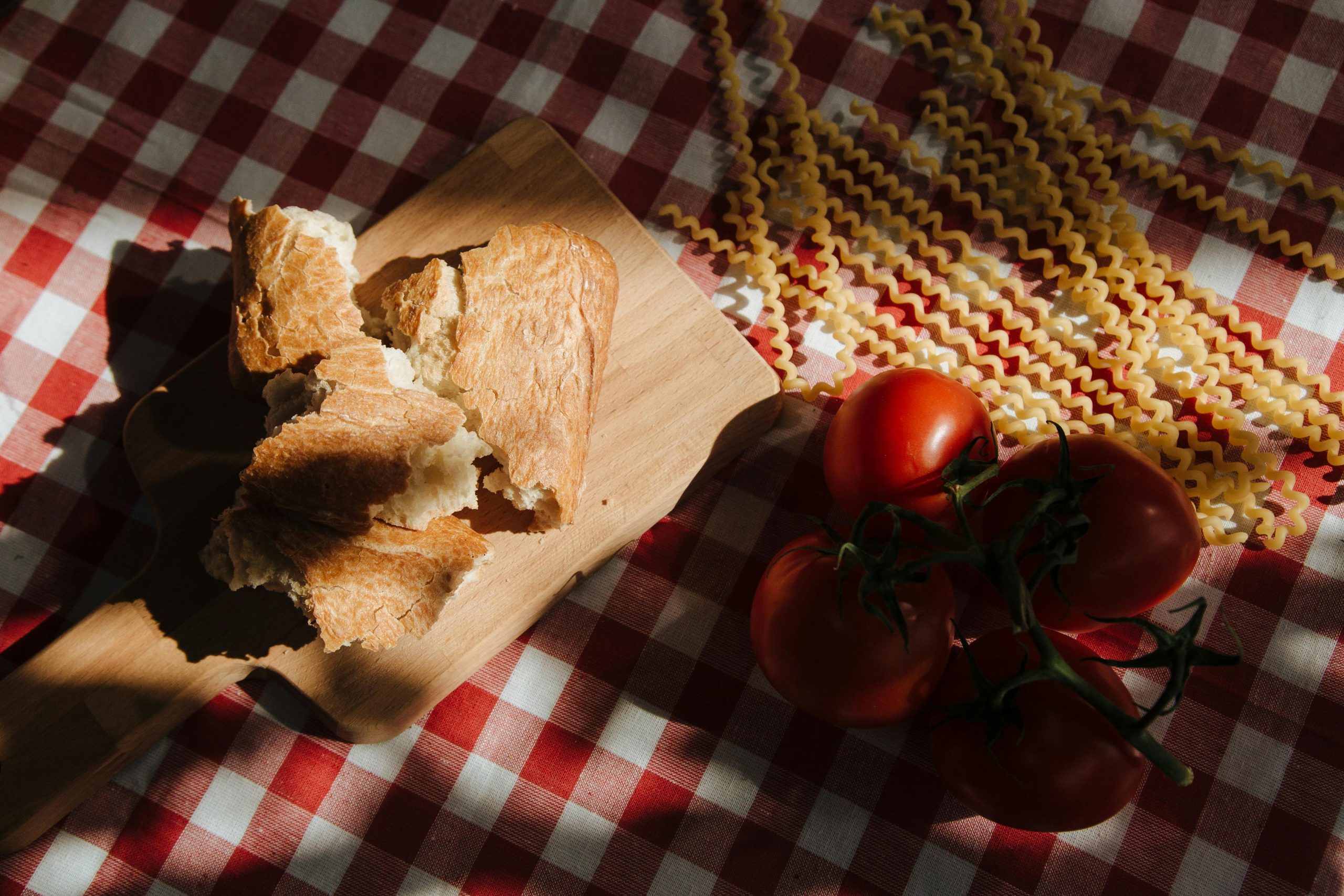 Bread and pasta on a checked red and white tablecloth with tomatoes on the table