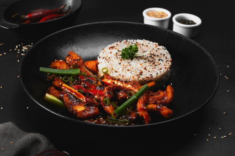 A black plate with a stir fry inside with some rice