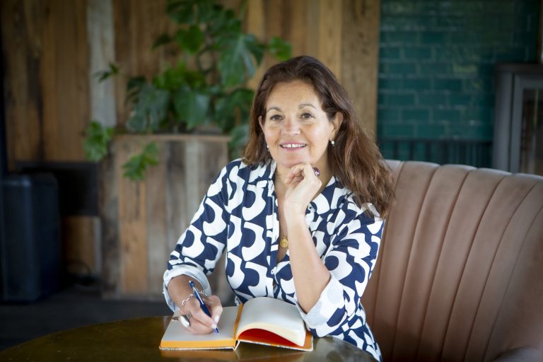 Nathalie in a patterned dress sitting writing in a notebook thinking pensively